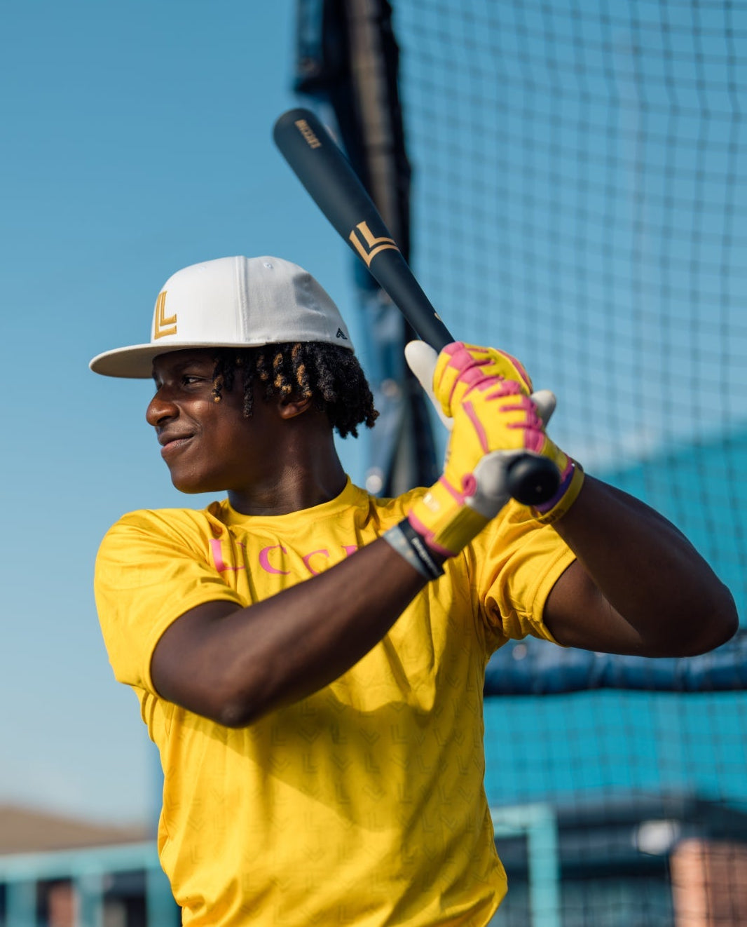 Person in yellow shirt and white cap holding a baseball bat on a clear day