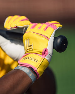 Close-up of a person wearing yellow and pink gloves with a brand logo, holding a sports ball.
