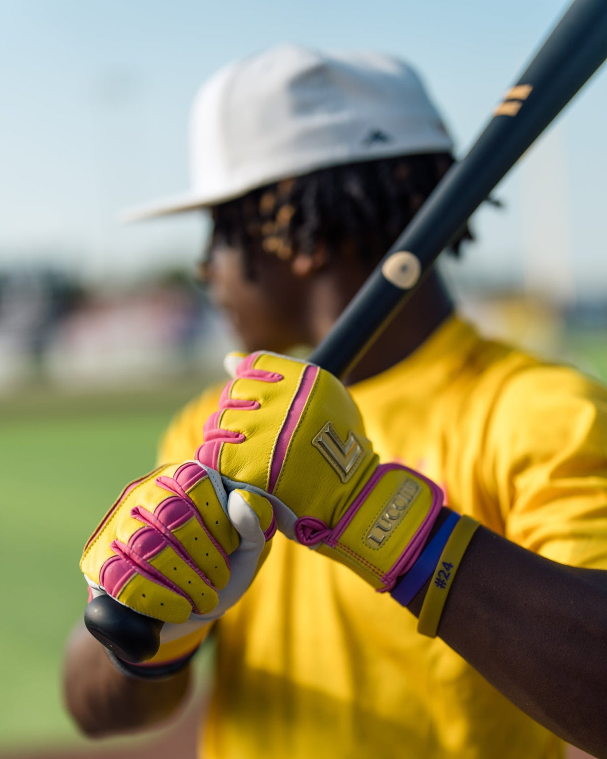 Person holding a baseball bat with a yellow glove on a blurred sports field background