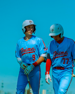 Two baseball players in blue uniforms with 'Prime' on their jerseys walking together against a clear blue sky.
