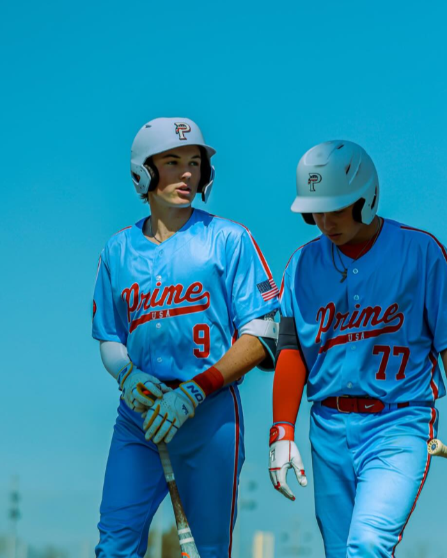 Two baseball players in blue uniforms with 'Prime' on their jerseys walking together against a clear blue sky.